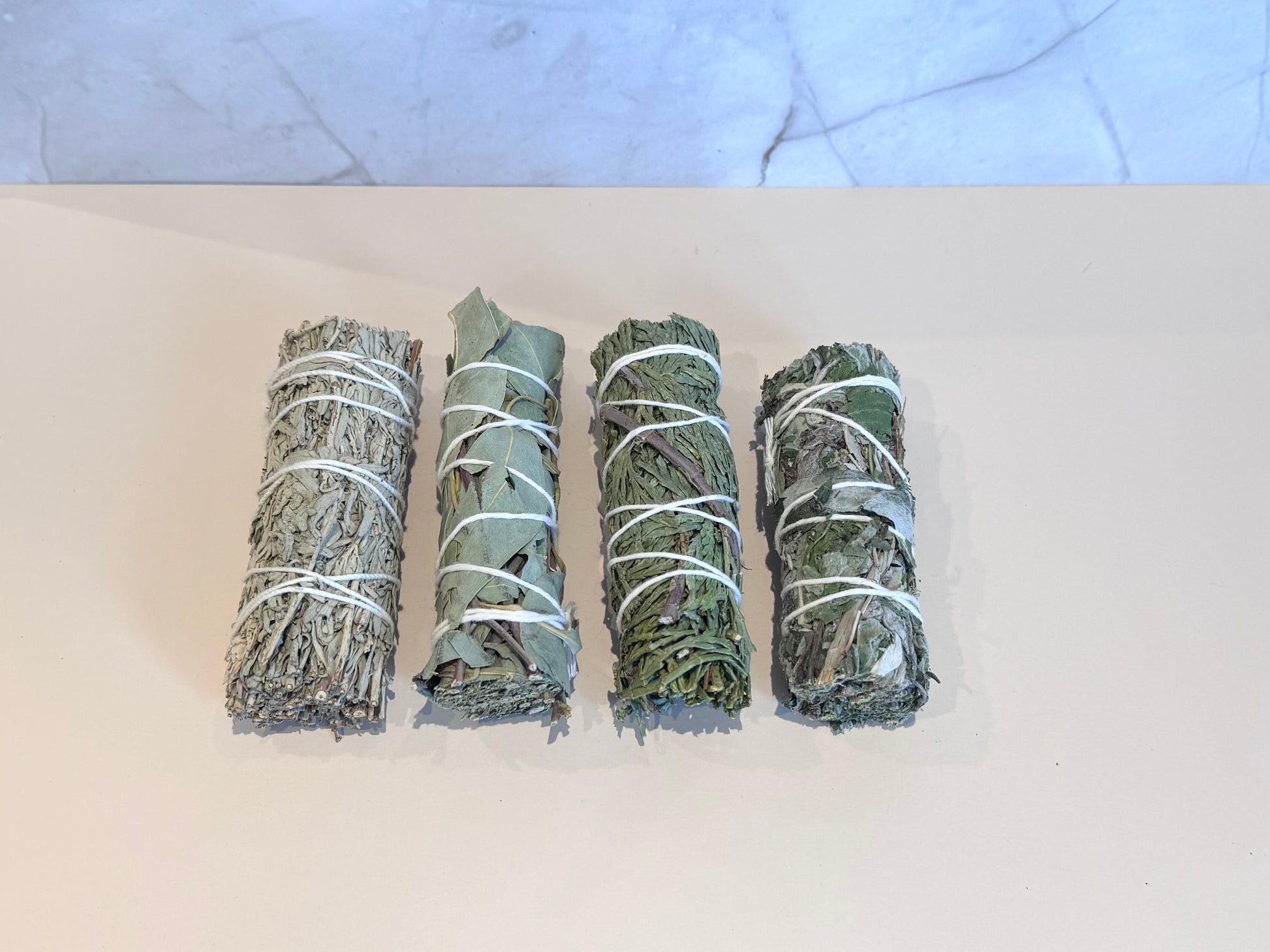 Box of smudge sticks, Blue Sage, Eucalyptus, Mugwort, Cedar with brand logo on a marble surface and ritual card. Gift set