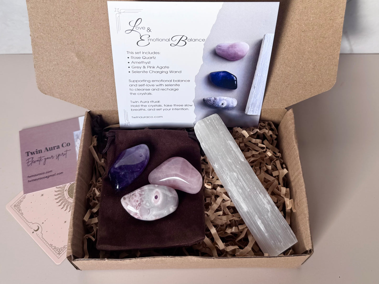 Box containing crystals: Amethyst, Rose Quartz, Grey and Pink Agate and a candle with a branded card on a beige background