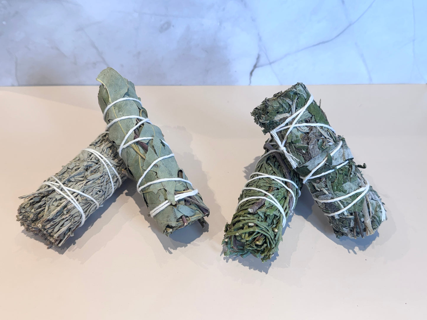 Box of smudge sticks, Blue Sage, Eucalyptus, Mugwort, Cedar with brand logo on a marble surface and ritual card. Gift set