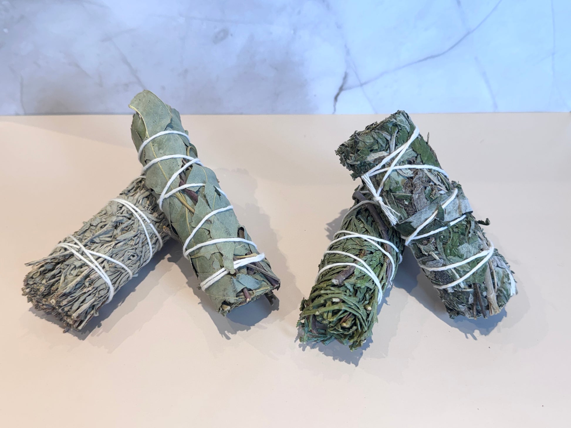 Box of smudge sticks, Blue Sage, Eucalyptus, Mugwort, Cedar with brand logo on a marble surface and ritual card. Gift set