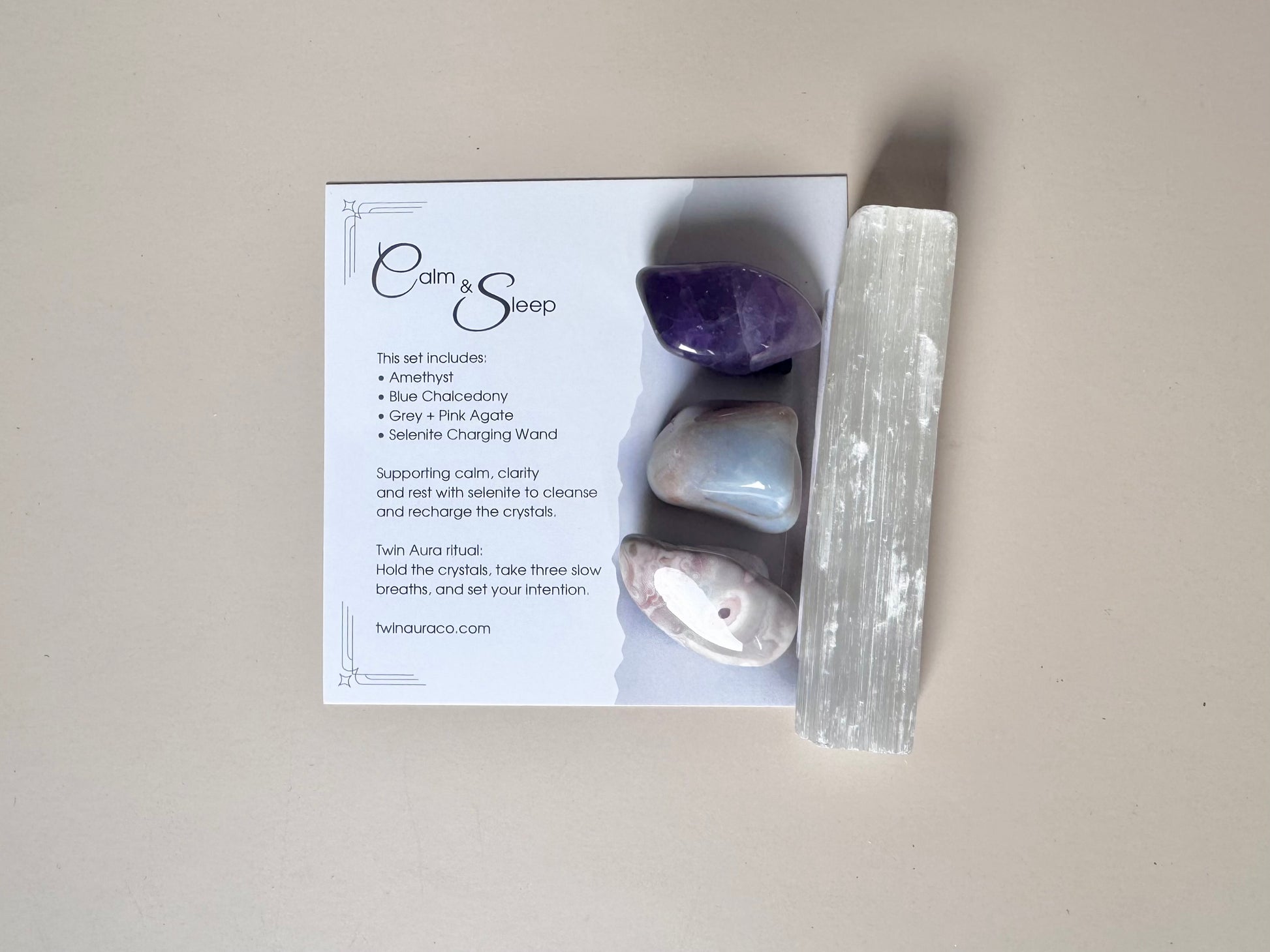 Box containing stones, a crystal, and a card with 'Calm & Sleep' branding on a neutral background. Amethyst, Blue Chalcedony, Grey and Pink agate, with Selenite wand and brown velvet bag. 