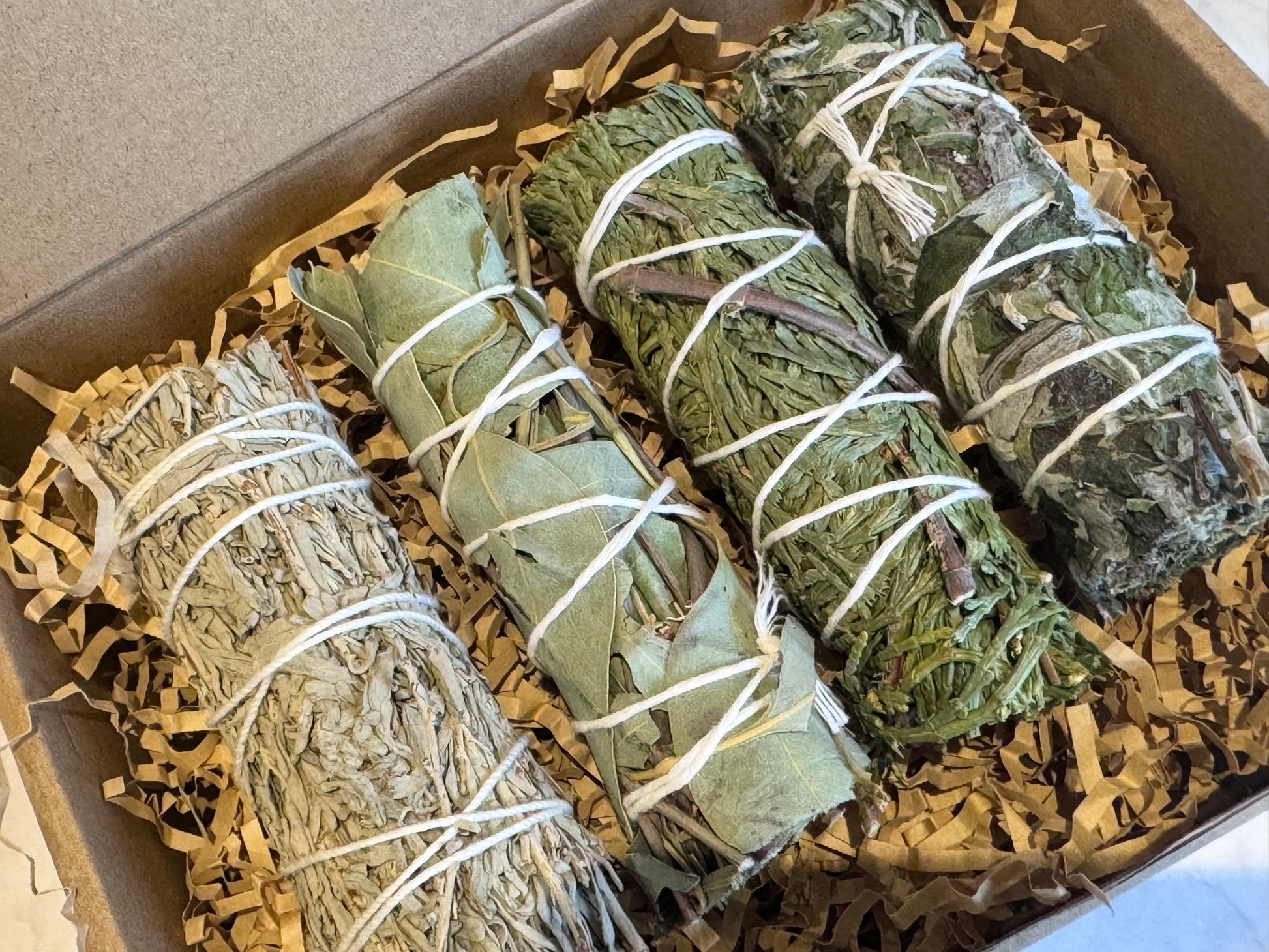 Box of smudge sticks, Blue Sage, Eucalyptus, Mugwort, Cedar with brand logo on a marble surface and ritual card. Gift set
