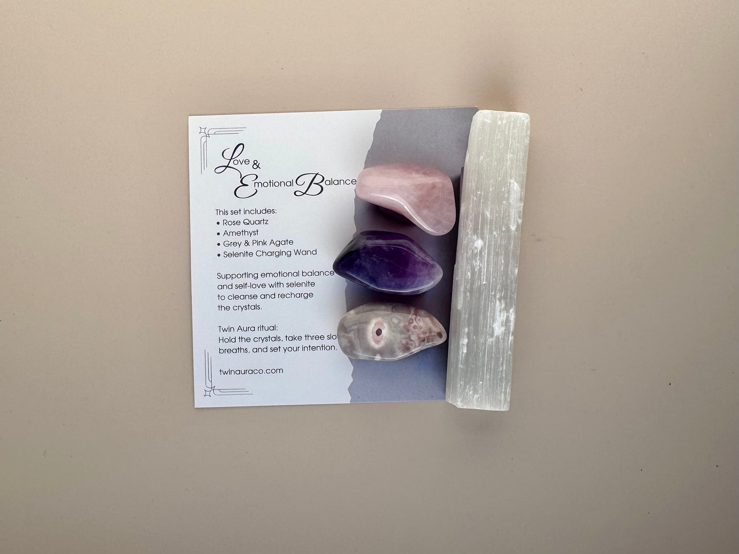 Box containing crystals: Amethyst, Rose Quartz, Grey and Pink Agate and a candle with a branded card on a beige background