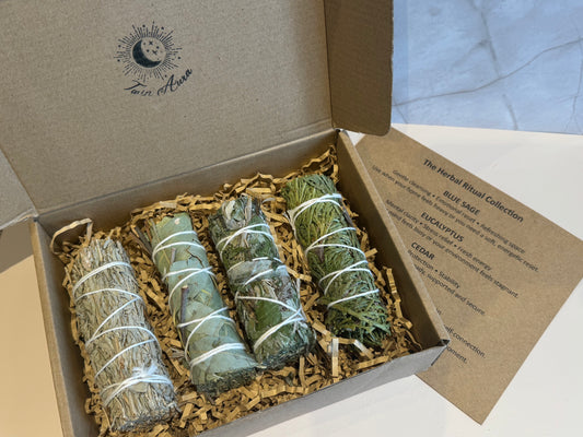 Box of smudge sticks, Blue Sage, Eucalyptus, Mugwort, Cedar with brand logo on a marble surface and ritual card. Gift set
