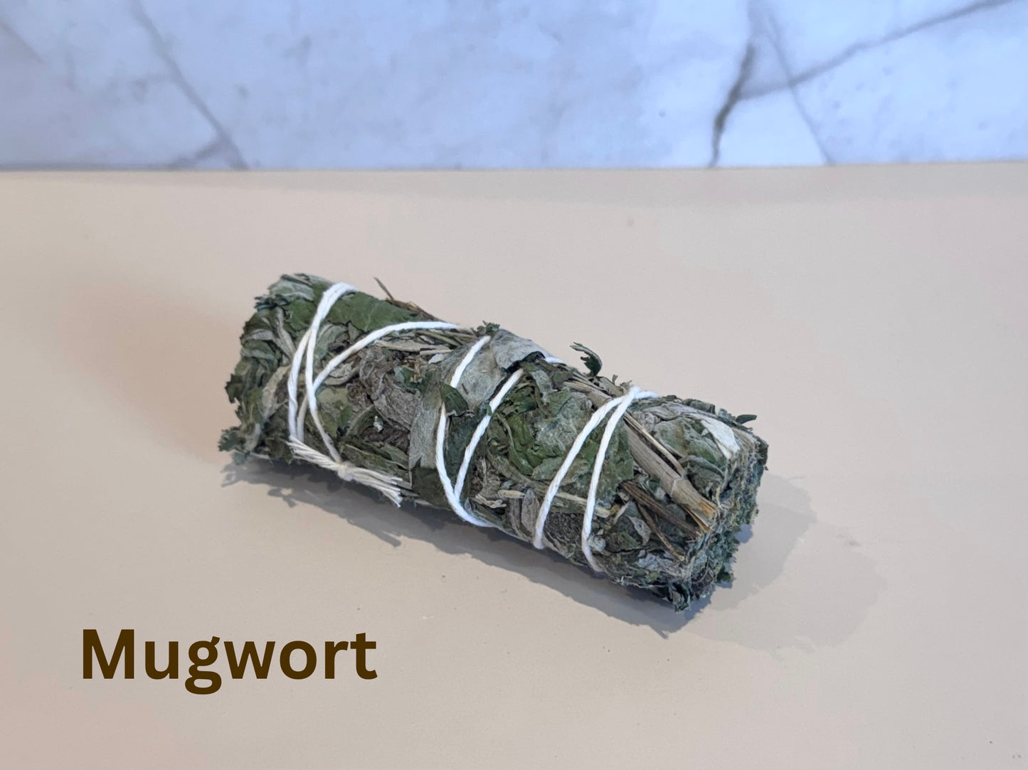 Rolled mugwort bundle smudge tied with twine on a light surface, with 'Mugwort' text below.